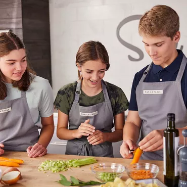 teen girls and boy peeling and chopping vegetables in kitchen