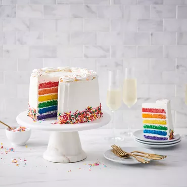 Rainbow layer cake with white frosting and sprinkles