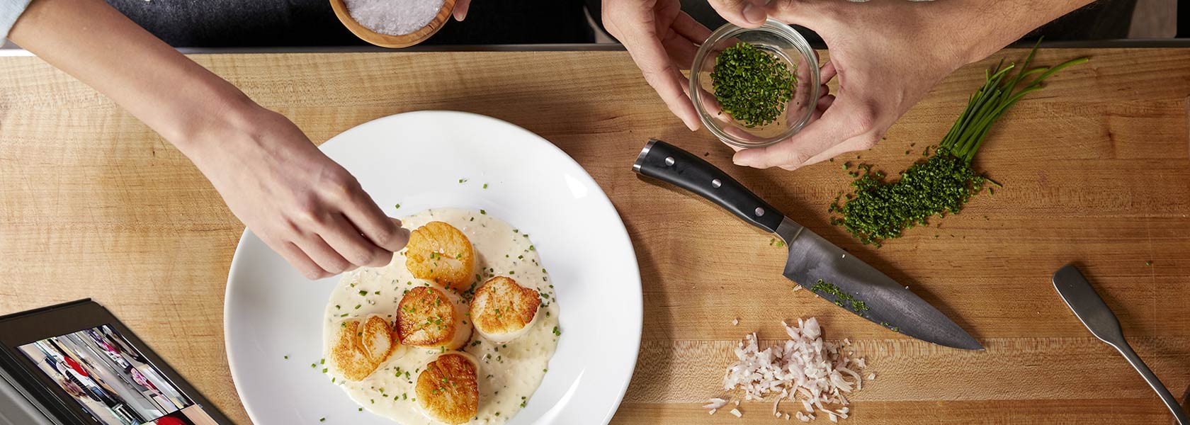 two chefs seasoning sea scallops with herbs