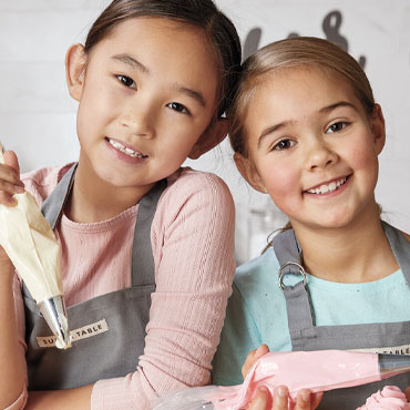 two girls in kitchen frosting cupcakes