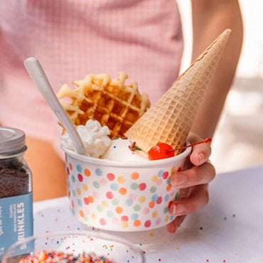 Child holding cup with ice cream and cone, with sprinkles on the side