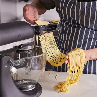 Homemade Spaghetti noodles being cut in KitchenAid pasta attachment