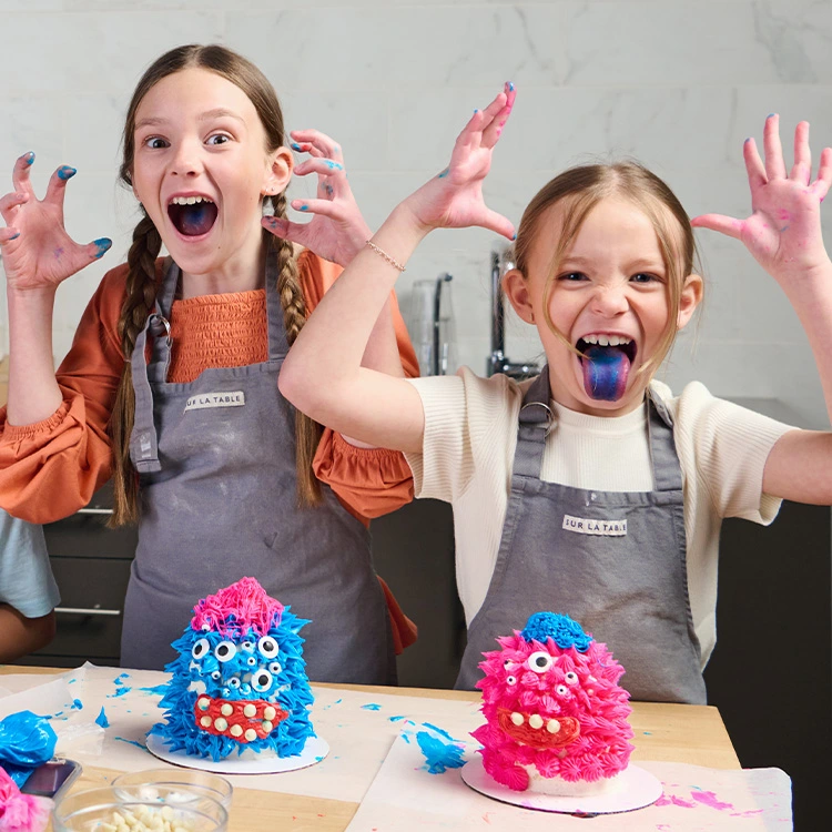 Two girls in gray aprons decorating monster cakes