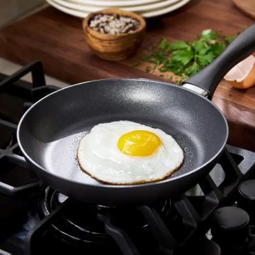 Nonstick skillet with black handle, frying an egg on cooktop