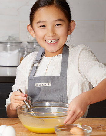 child whisking eggs in a glass bowl