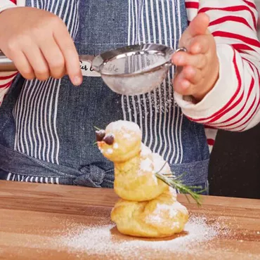 Child dusting snowman with powdered sugar