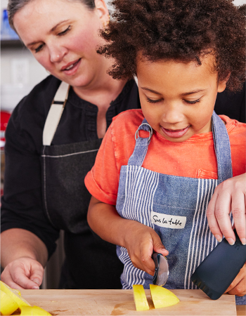 chef assisting child in slicing bell pepper