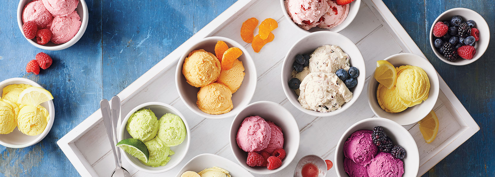various colorful ice creams in white bowls with fresh fruit