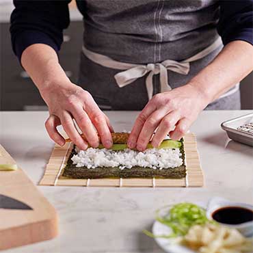chef hands making sushi roll on bamboo mat