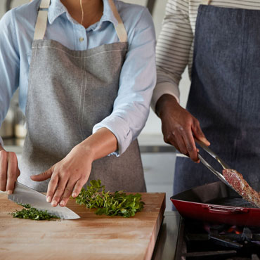 hands chopping herbs and searing steak in cast iron grill pan